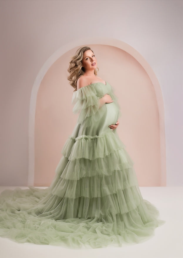 Pregnant mother wearing green dress standing in front of boho arch